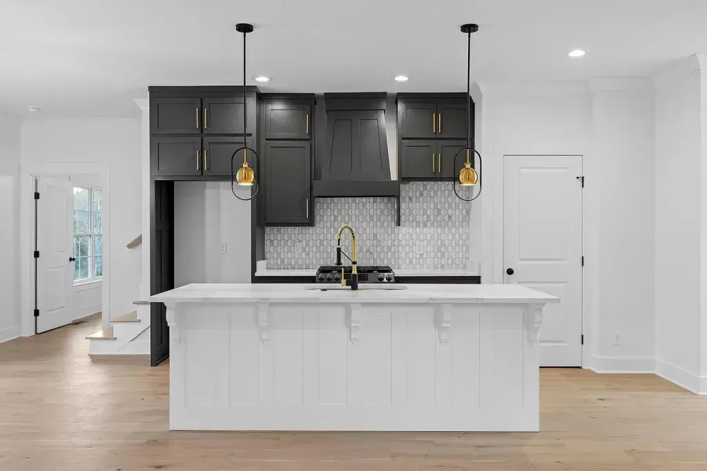 Kitchen with dark upper cabinets, a white paneled island, gold pendant lights, and a patterned tile backsplash
